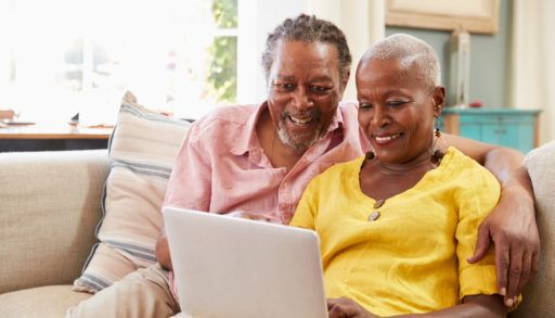 Senior Couple Sitting On Sofa Using Laptop to access the internet At Home Together