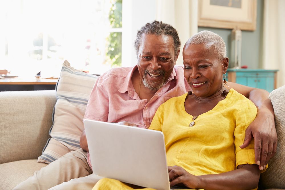 Senior Couple Sitting On Sofa Using Laptop to access the internet At Home Together
