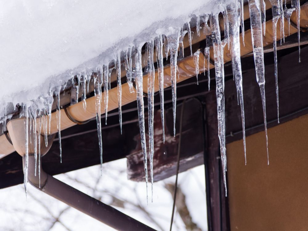Sharp icicles and melted snow hanging from eaves of roof. Beautiful transparent icicles slowly gliding of a roof
