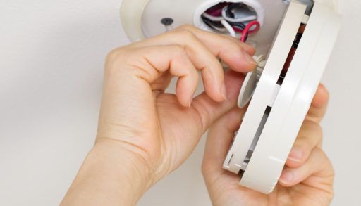 Horizontal photo of female hands taking home smoke detector apart with white ceiling background