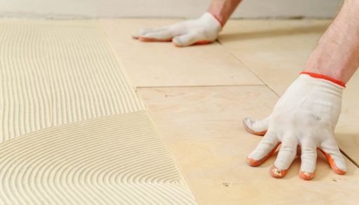 A close-up of gloved hands laying plywood on top of subflooring