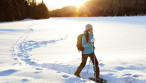 Winter sport activity. Woman hiker hiking with backpack and snowshoes snowshoeing on snow trail forest in Quebec, Canada at sunset. Beautiful landscape with coniferous trees and white snow.