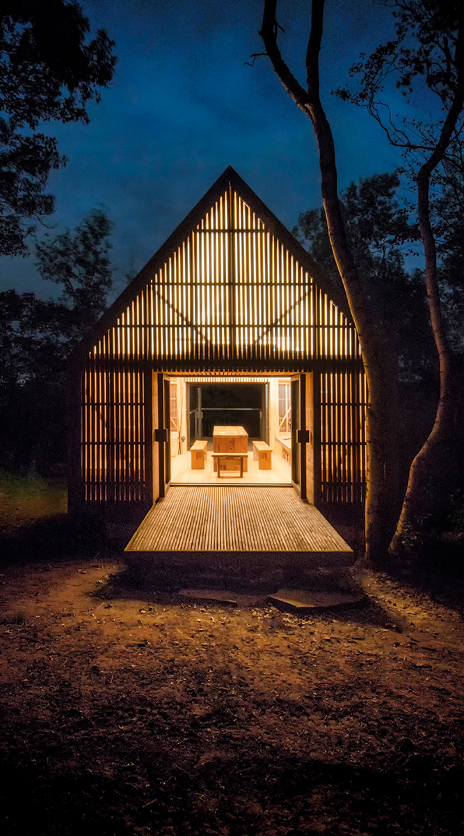wooden slat cottage lit from within at night, colin and justin's escapology