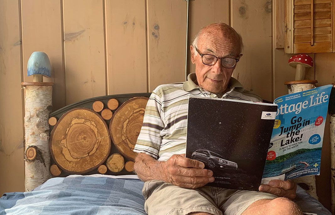 Jim Curtis laying on a bed and reading a Cottage Life magazine in front of his mushroom and birch headboard project