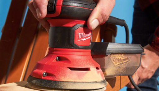 man using a random orbital sander to sand a muskoka chair on a blue background
