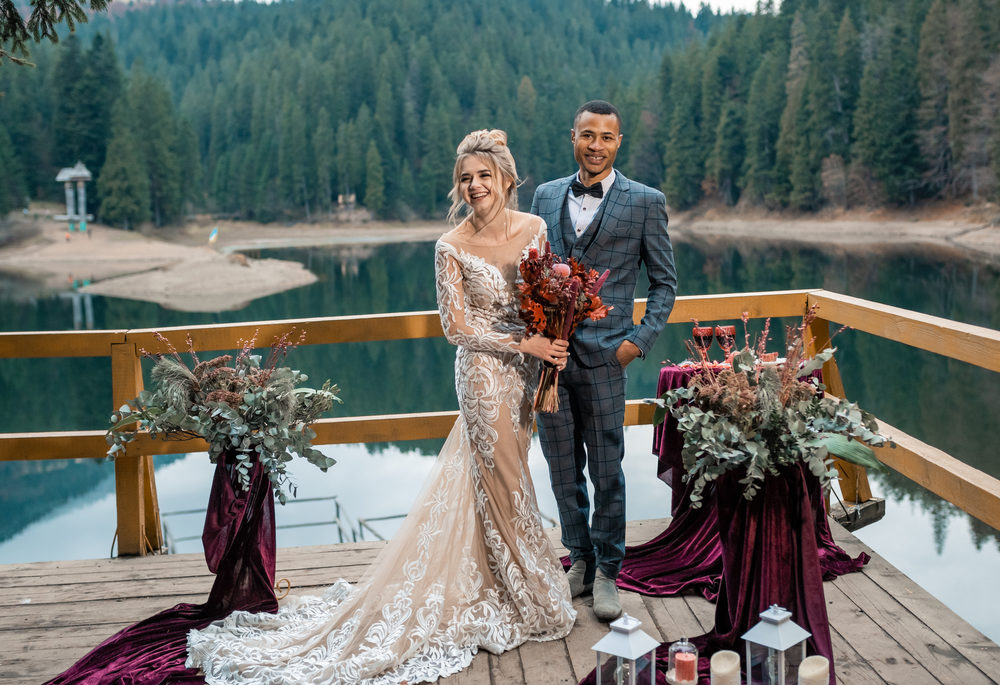 A bride and groom standing on a deck overlooking a lake