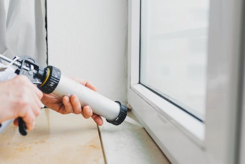 Hands of worker using a silicone tube for repairing of window indoor