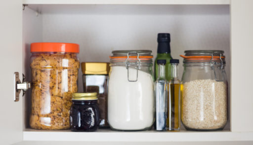 stocked kitchen cupboard with food - jars and containers of cereals, jam, coffee, sugar, flour, oil, vinegar, rice