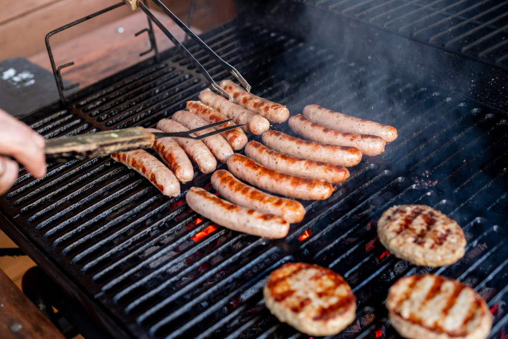 Man at a barbecue grill with smoke.Grilling sausages on barbecue grill. BBQ party.Delicious german sausages or bratwurst