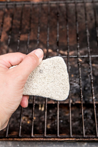 Using natural pumice stone to scrub charred food deposits and rust from BBQ grill metal grid. Safe way to clean grill concept. barbecue tune-ups