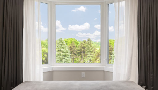 A large bay window with a view of greenery and drapes to the sides