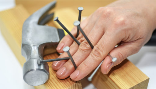 A close-up of a hand, a hammer, and several nails