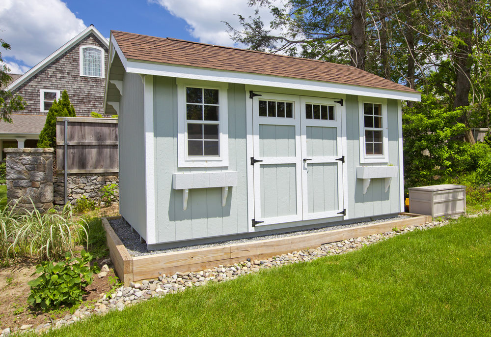 A blue-grey garden shed sitting on gravel