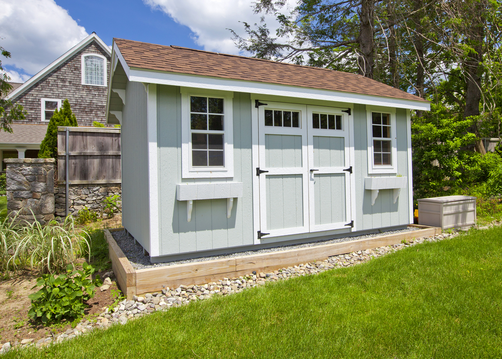 A blue-grey garden shed sitting on gravel
