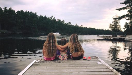 Three kids sitting at the end of a dock