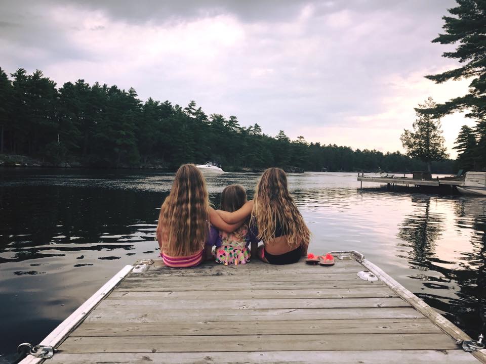 Three kids sitting at the end of a dock