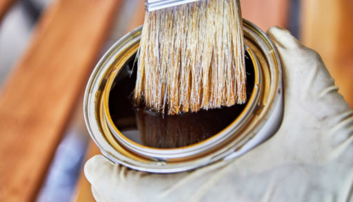 A man's gloved hand holding a can of stain