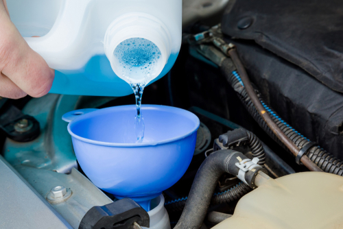 Man hands filling blue washer fluid in car tank through funnel from plastic bottle for windshield in garage. Care about automobile. Closeup. Front view. emergencies