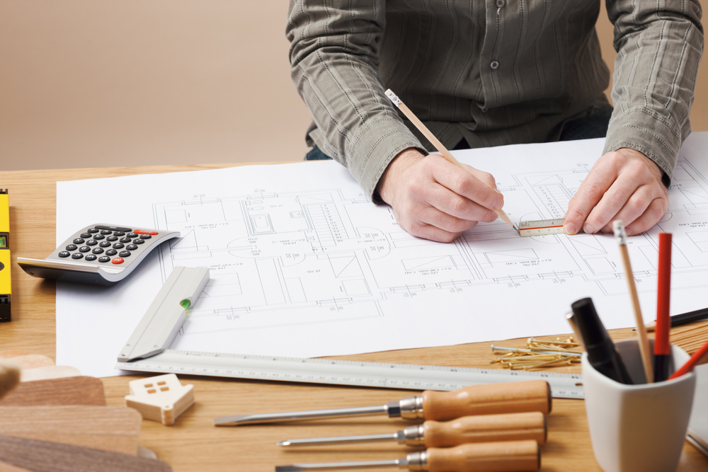 Professional architect and construction engineer working at office desk hands close-up, he is drawing on a building project with a pencil and a ruler, shed plans