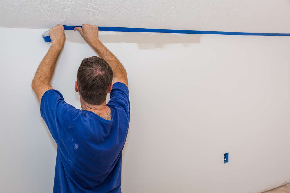 Man putting blue painter's tape on the ceiling, painting