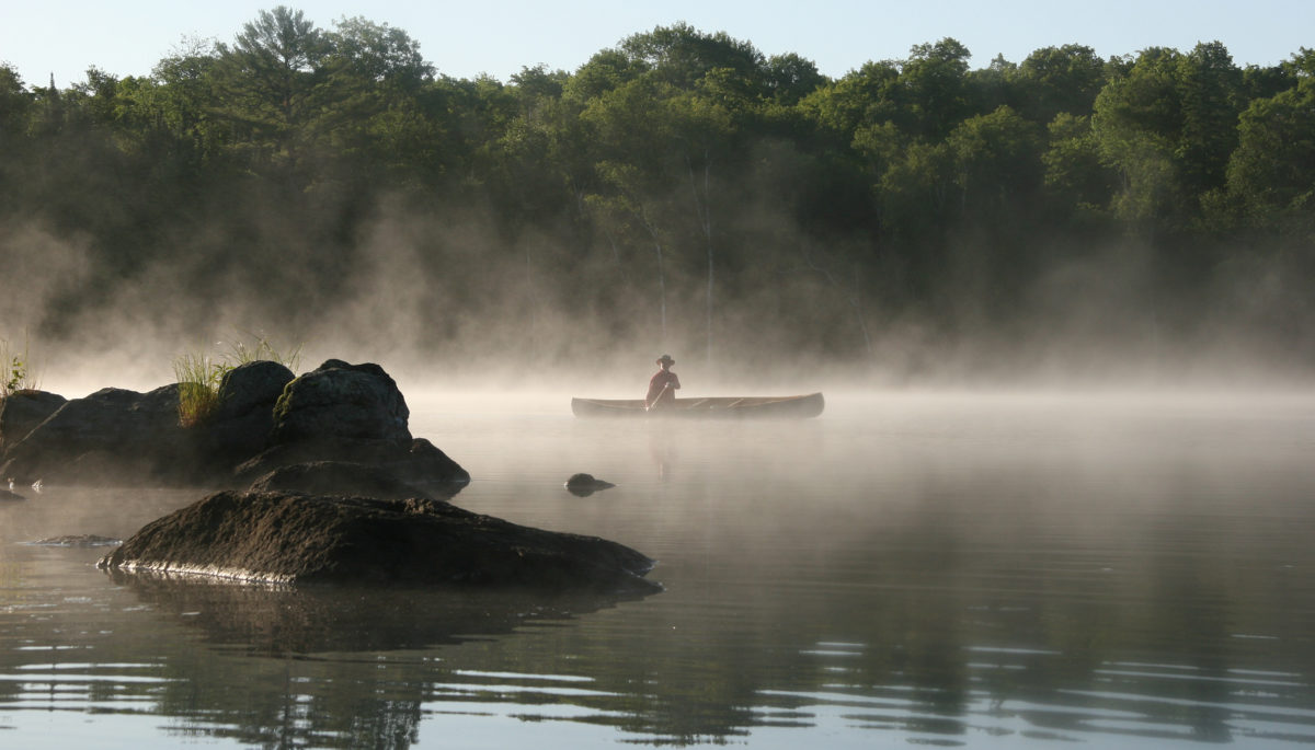 A person canoeing on a Misty Lake in the Haliburton Highlands.