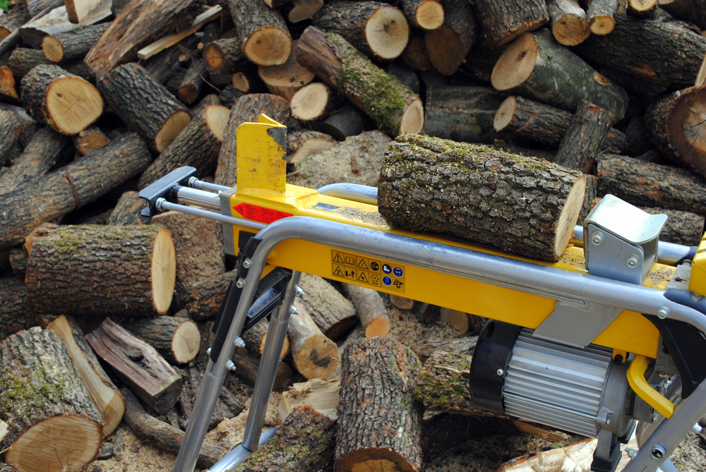 A yellow log splitter against the background of a woodpile