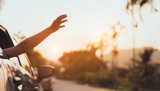 car driving at sunset with a passenger sticking their hand out of the back window