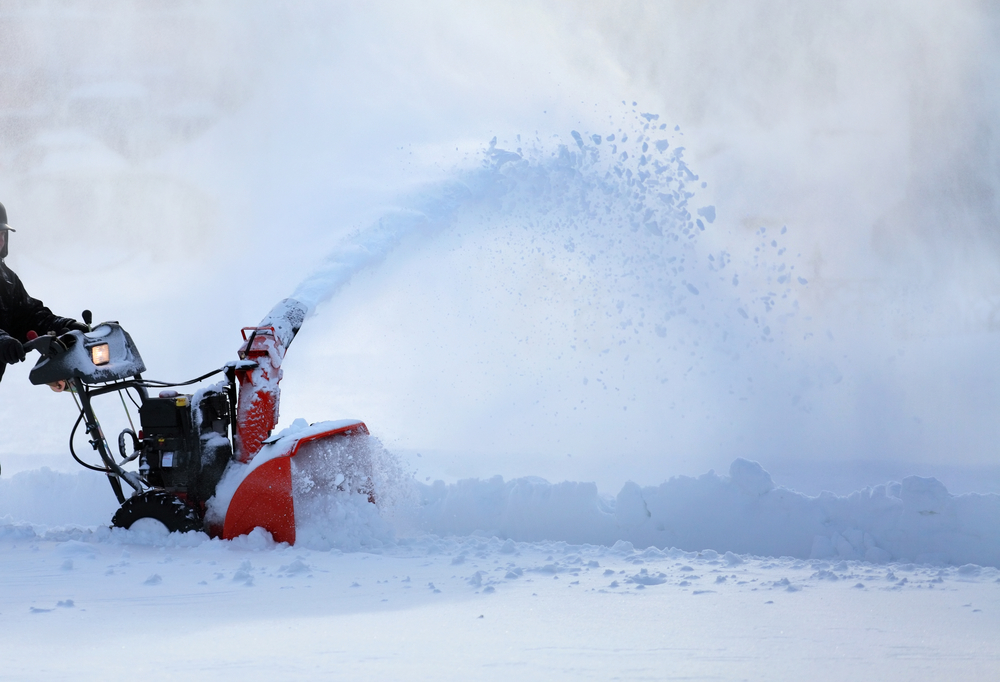 A pair of hands pushing a snow blower through deep snow