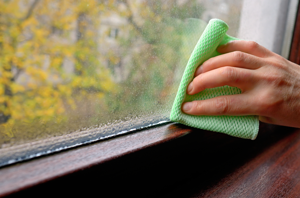 A hand wiping a wet windowsill with a green cloth