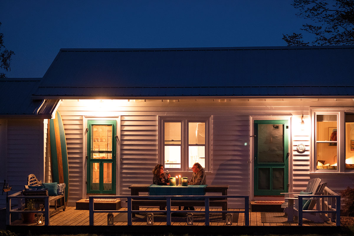 Pauline and Robbie sit on their deck at night drinking wine, lit by candlelight