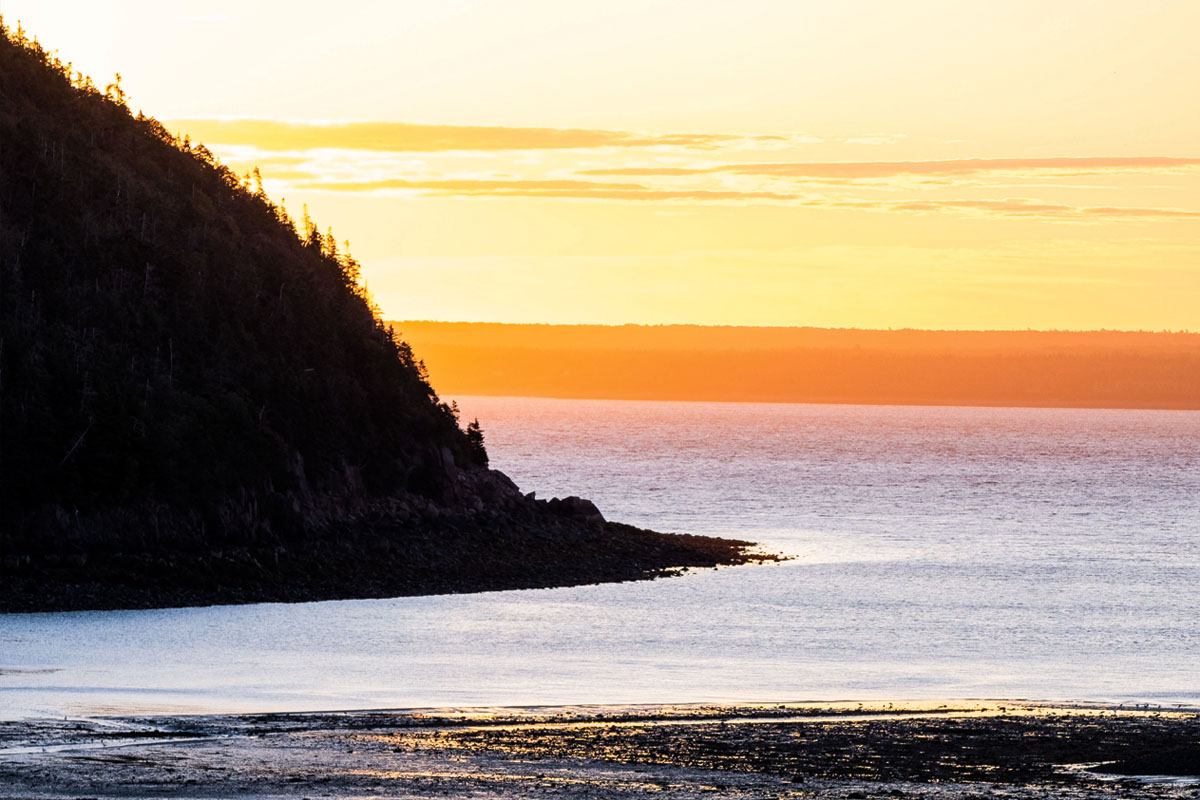 the sun setting on St. Mary's Bay as someone harvests soft-shell clams