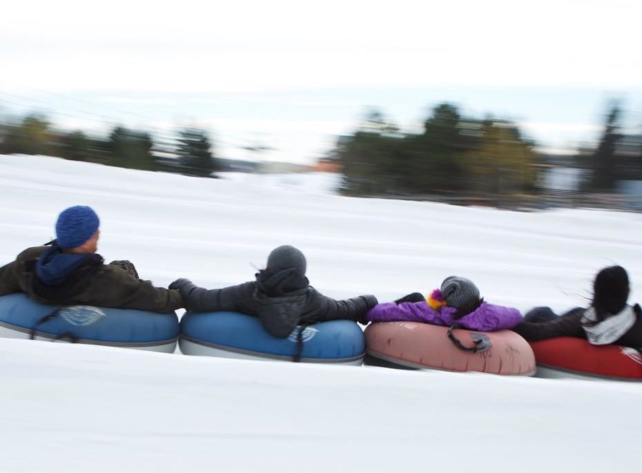 People holding onto each other while snow tubing