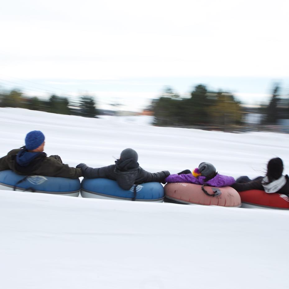People holding onto each other while snow tubing