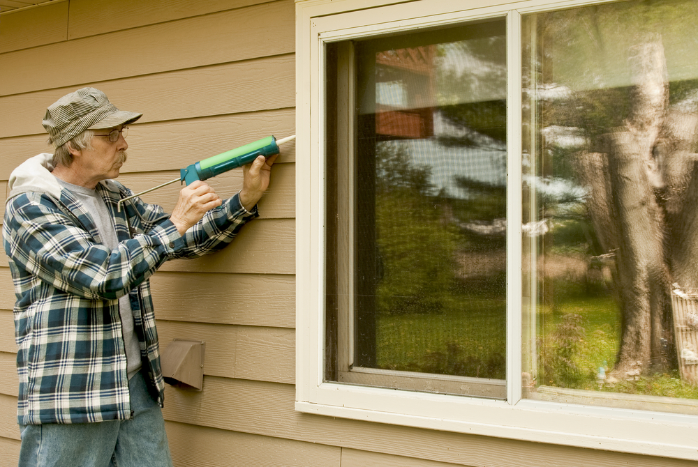 A man using a caulking gun to seal cracks around a large window