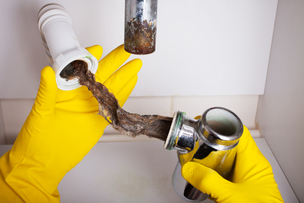 Close-up of yellow-gloved hands taking apart the under-cabinet plumbing