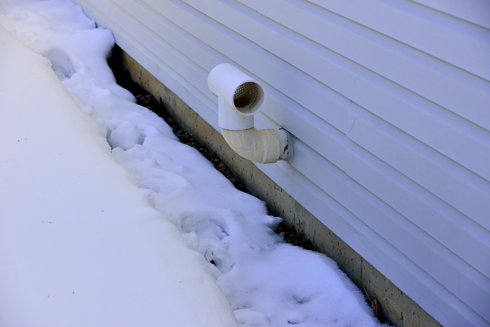 The exhaust vent on the side of a house shown clear from snow
