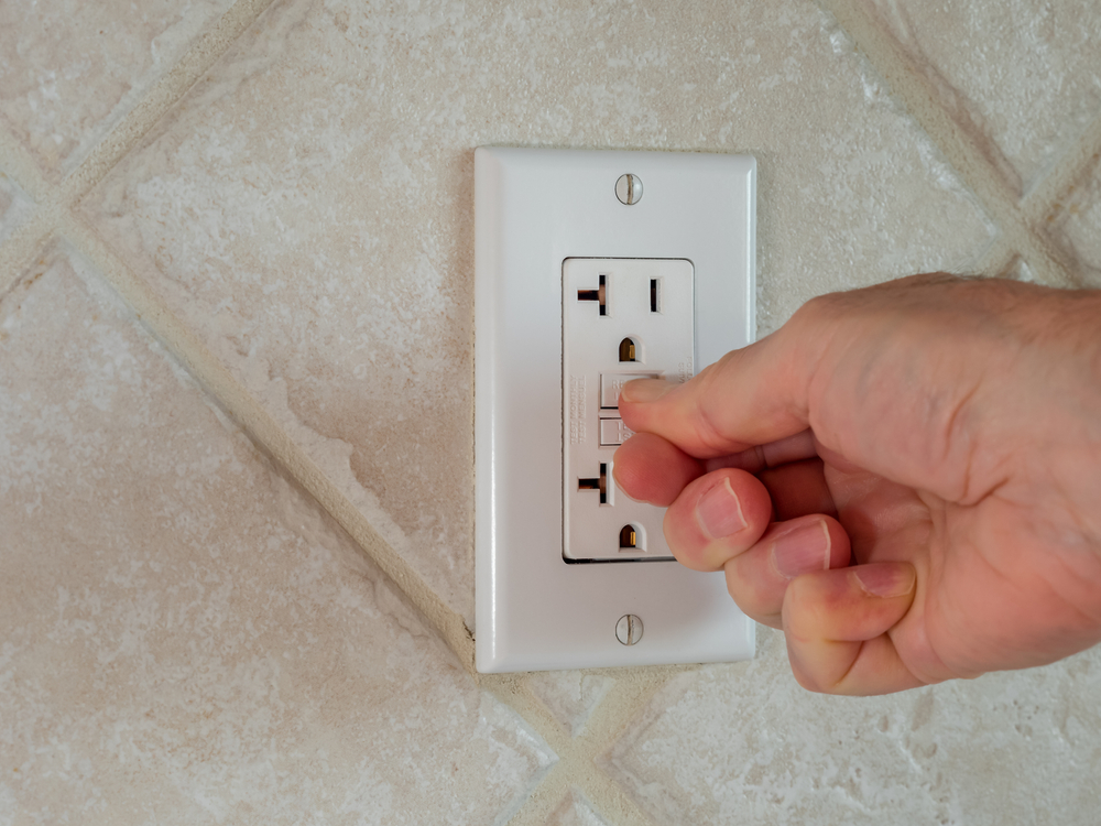 A hand replacing a GFCI on a wall plate