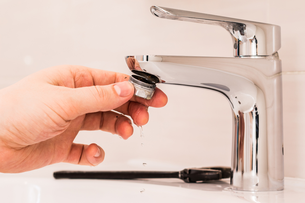 Close-up of a hand removing the aerator cap on a faucet
