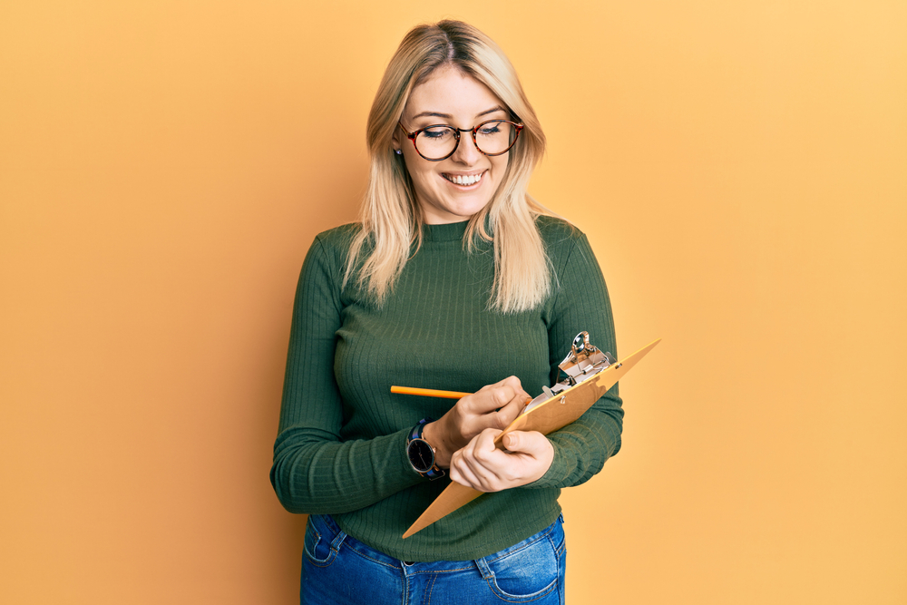 A young woman smiling as she writes on a clipboard