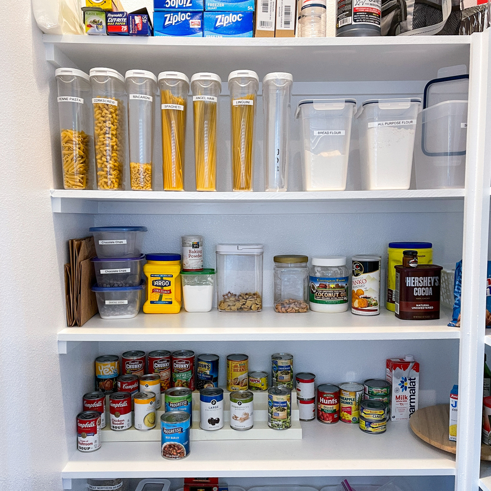 Four shelves of a tidy, organized pantry, filled with bottles and canned goods
