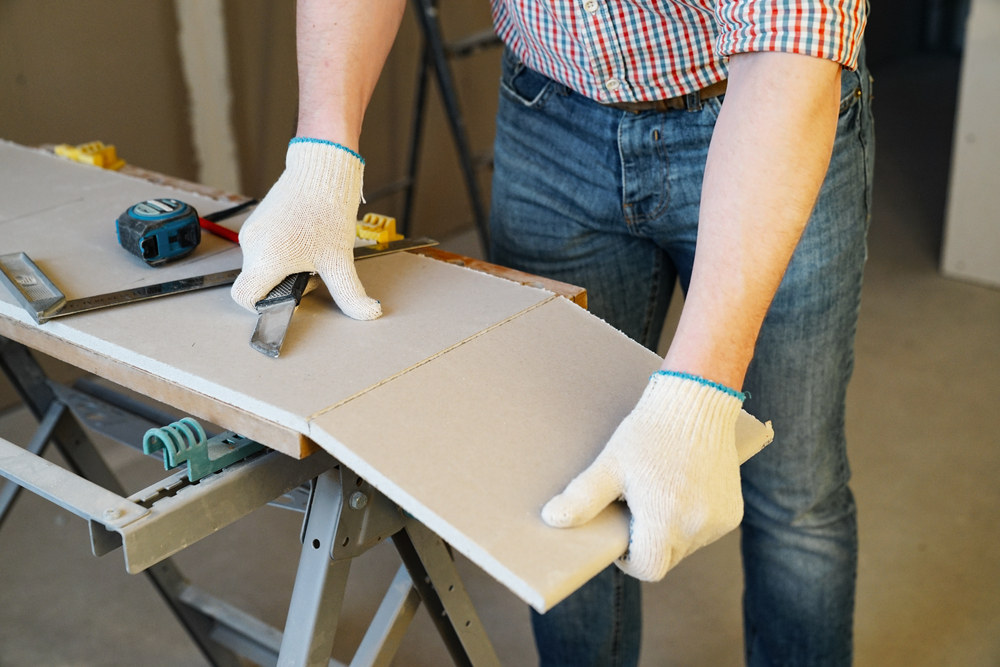 A man cutting a sheet of drywall with a knife