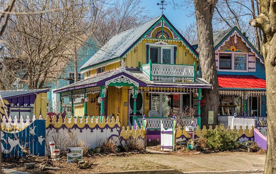 Colourful cottage with yellow exterior and purple, turquoise, and white trim. Gingerbread-style woodcarvings throughout.