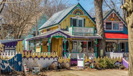 Colourful cottage with yellow exterior and purple, turquoise, and white trim. Gingerbread-style woodcarvings throughout.