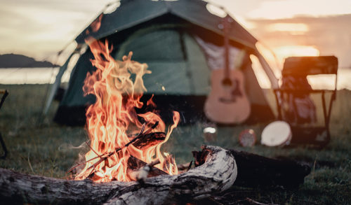 A campsite with a lit fire and a tent, guitar, and chair just behind it.