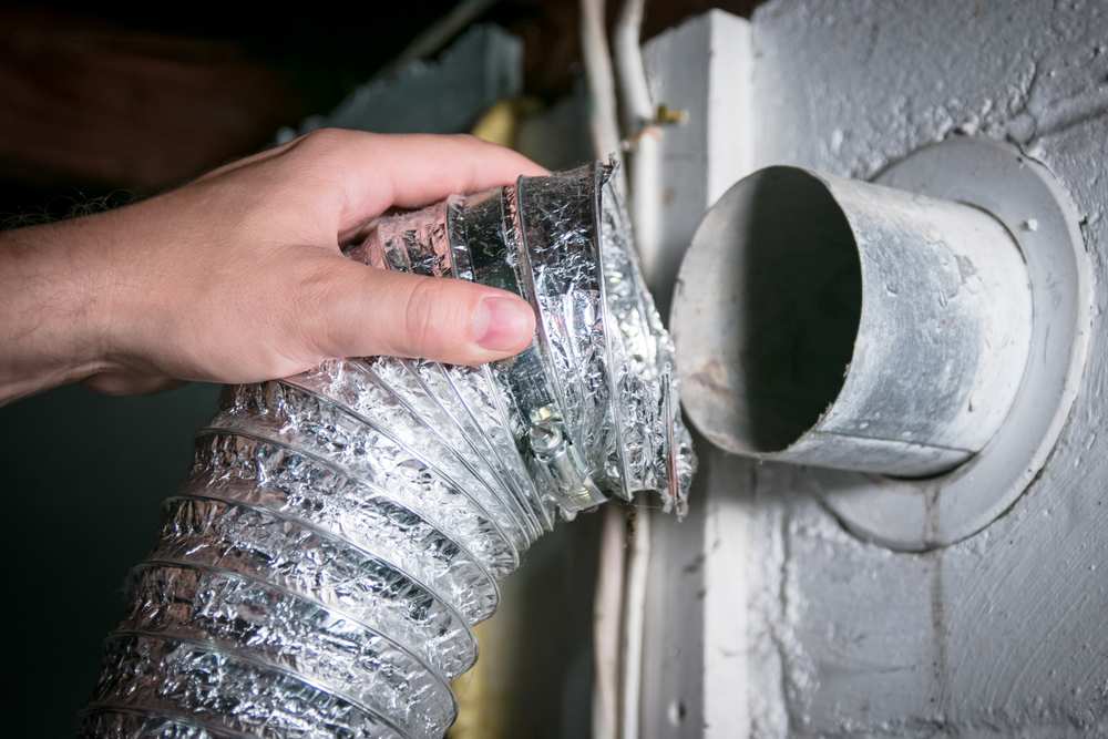 Closeup of a hand removing an aluminum dryer vent hose