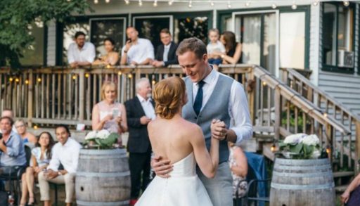 A couple dancing, dressed in wedding attire, outside in front of a cottage. Guests watching them in the background.