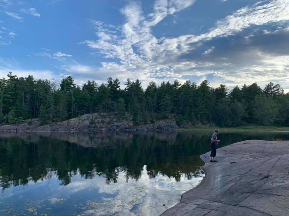 Trees along a shore, with their reflection in a still lake.