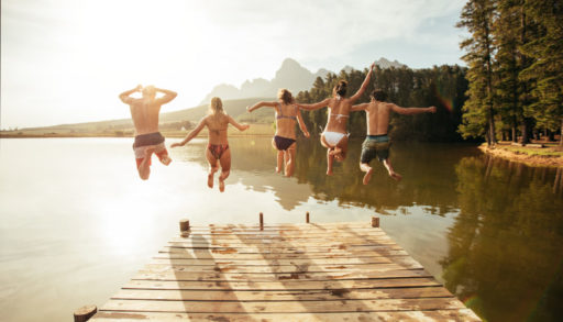 Friends jumping off a dock into a lake in the summer.