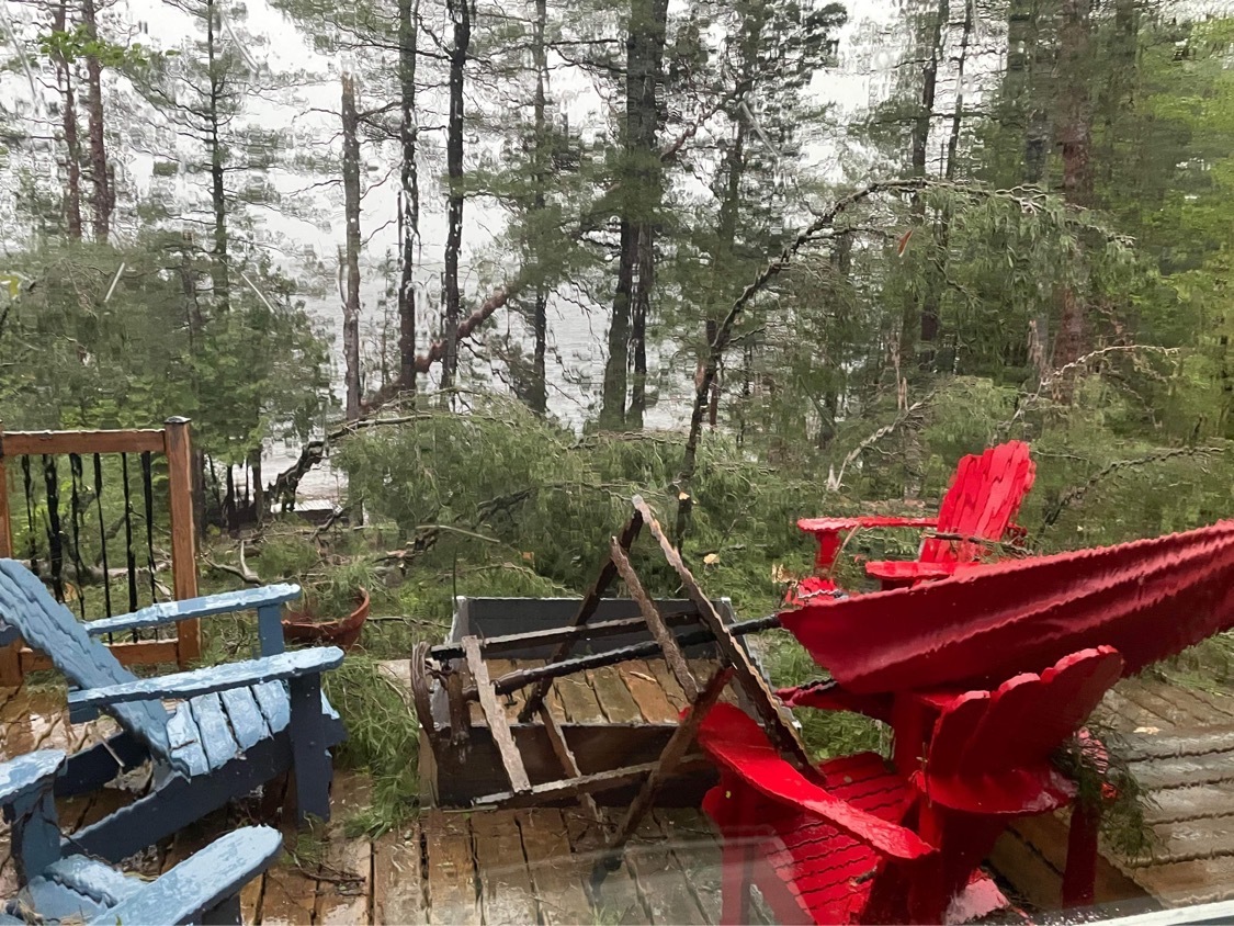 A table flipped and trees bending in heavy winds and rain, from out a window.