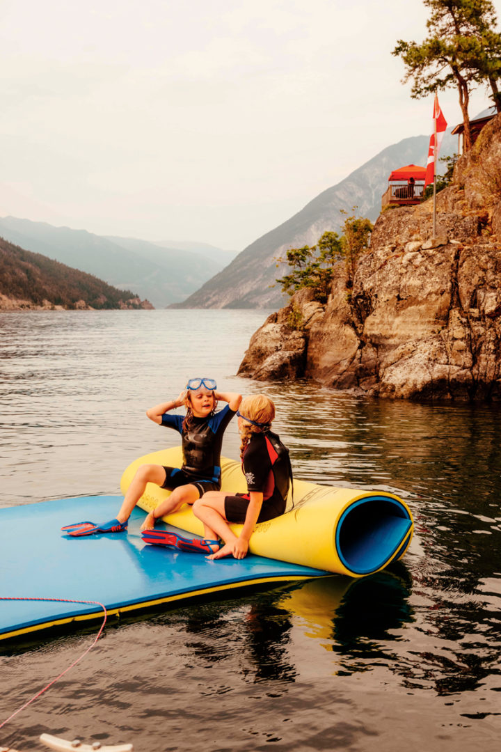 Two children play on a floater mat on the lake